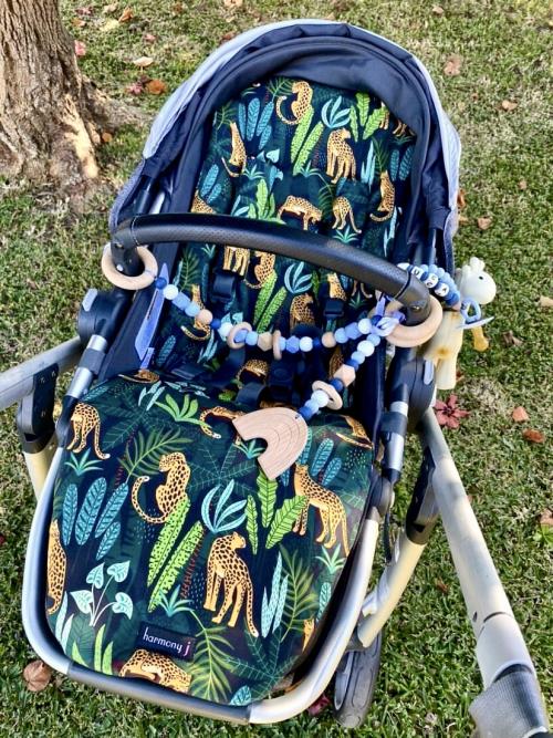 A printed animal custom pram insert with a beaded baby toy hanging from the pram handle bar