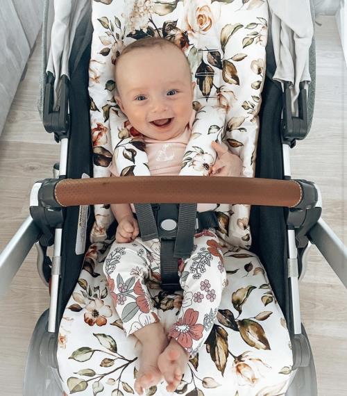 A baby girl in her pram featuring the Bouquet in White fabric pram liner